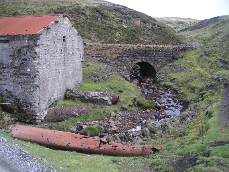 mc_compressorhouse3.jpg - Entrance of the water pipe into the house, buried exit on the right hand side at the bottom of the slope with the bridging section by the road.