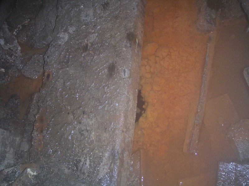 ccl_middlecleugh_sump3.jpg - Middlecleugh Sump, realising that there was no solid floor, we had been walking on timbers over the sump. The dark between the beam and orange sludge is flooded sump.